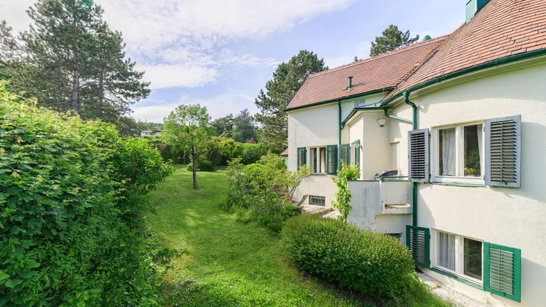 Seitlicher Blick auf das Haus mit grünen Fensterläden und einem weitläufigen, gepflegten Gartenbereich.