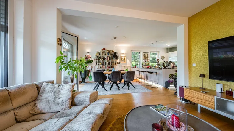 Helles, offenes Wohnzimmer mit beigem Sofa, Holzboden und Blick auf den Essbereich und die Küche.