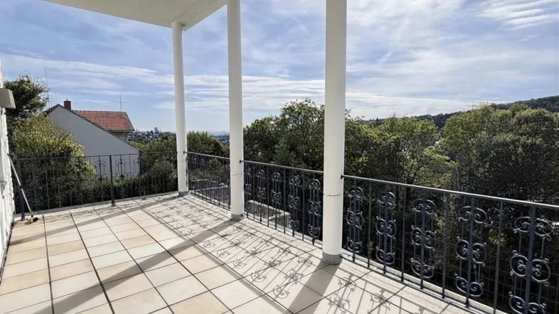 Geräumige Terrasse mit Fliesenboden, dekorativem Geländer und weitem Blick ins Grüne.
