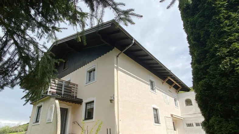 Charmantes Landhaus mit beiger Fassade, Satteldach und kleinem Balkon, umgeben von Grünflächen.