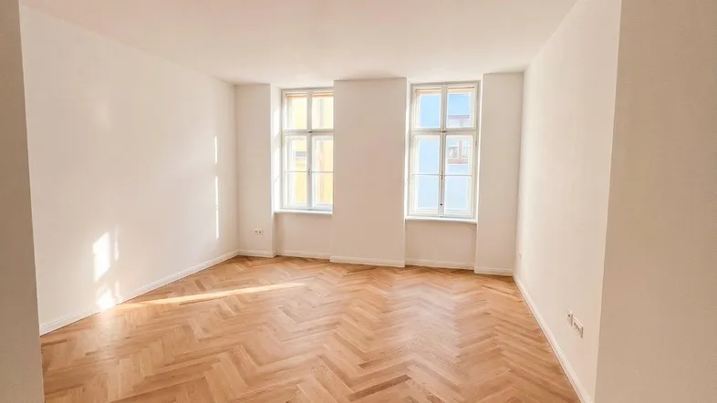 Helles Zimmer mit Fischgrätparkett und zwei großen Fenstern, ideal als Wohn- oder Schlafzimmer.