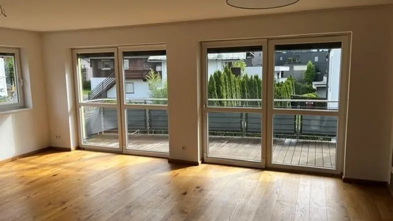 Helles Wohnzimmer mit Holzboden und großen Fenstern, die auf einen Balkon führen.