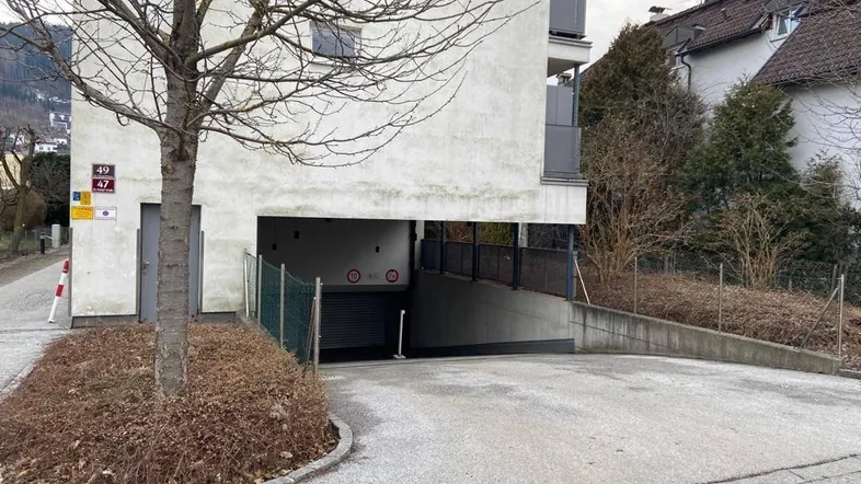 Eingang zur Tiefgarage eines modernen Wohngebäudes mit Zufahrt und umliegender Vegetation.