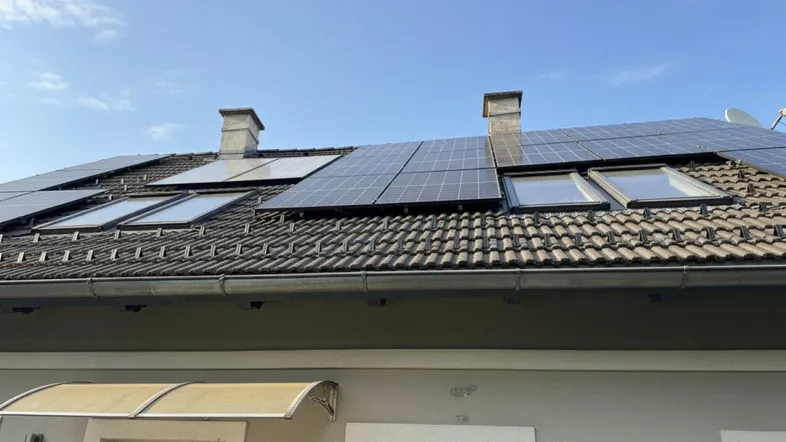 Dachansicht eines Hauses mit Photovoltaikanlage und Dachfenstern unter blauem Himmel.