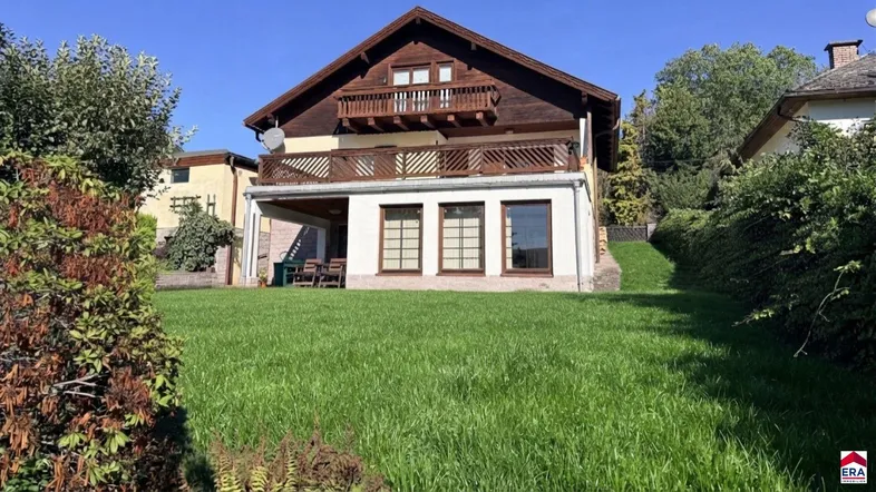 Großzügiger Gartenbereich mit Rasenfläche und überdachter Terrasse vor dem Haus.