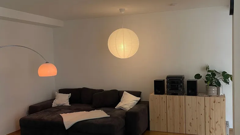 Gemütliches Wohnzimmer mit dunklem Ecksofa, Holzboden und moderner Beleuchtung.