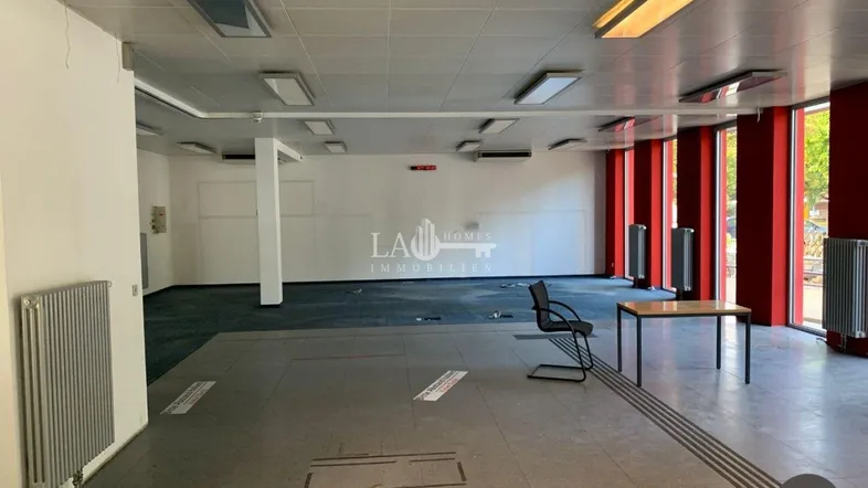 Geräumiger Gewerberaum mit großen Fenstern, Teppichboden und Fliesen, ideal für Büro oder Einzelhandel.