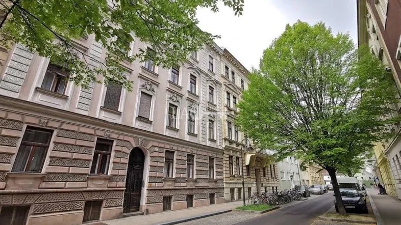 Historische Fassade eines Mehrfamilienhauses an einer ruhigen Straße mit Bäumen und parkenden Fahrrädern.