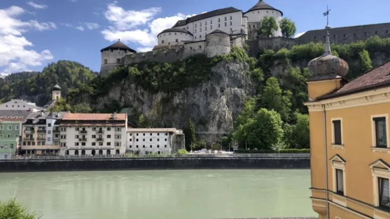 Historische Burg auf einem Felsen über dem Fluss mit umliegenden Gebäuden und blauem Himmel.