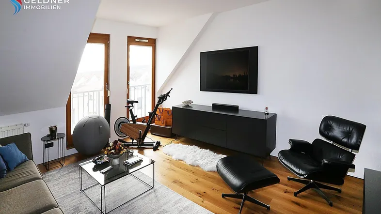 Helles Wohnzimmer im Dachgeschoss mit Holzboden, moderner Einrichtung und Zugang zum Balkon.