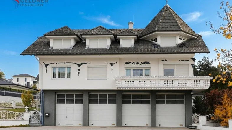 Großes Haus mit markantem Turmdach, Balkon und drei Garagentoren im Erdgeschoss.