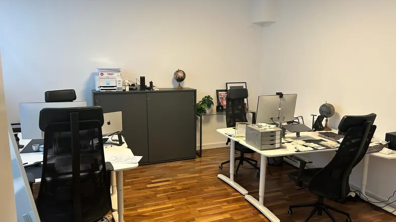 Geräumiges Büro mit mehreren Arbeitsplätzen, Holzboden und weißen Wänden, gut beleuchtet.