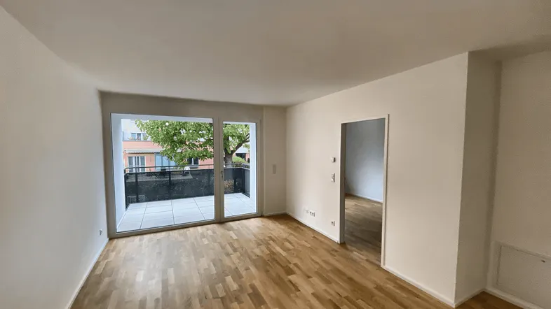 Helles Wohnzimmer mit Parkettboden und großen Fenstern, die Zugang zu einem modernen Balkon bieten.
