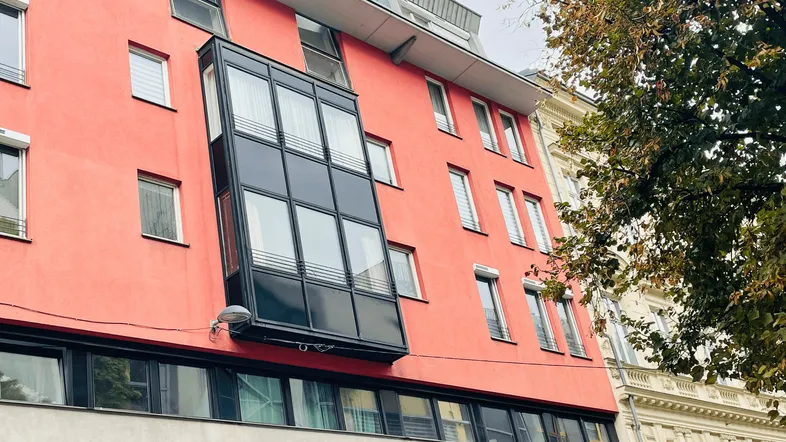 Moderne Fassade mit leuchtend rotem Putz und einem markanten Glaserker.