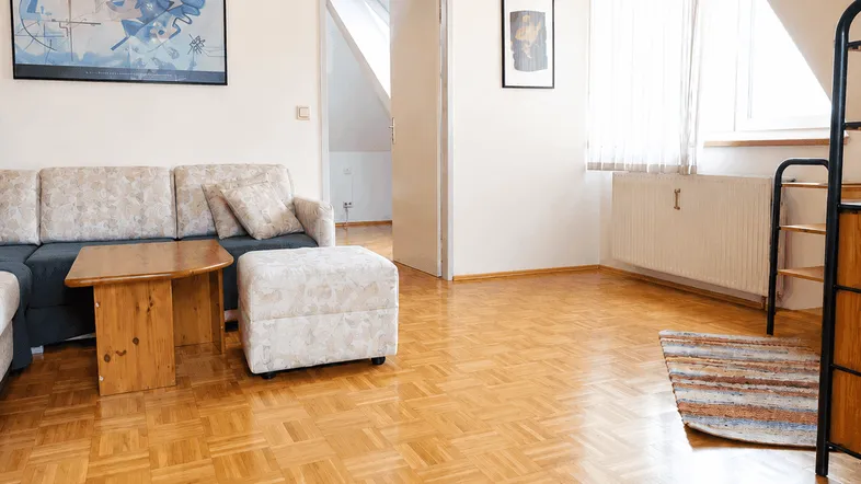 Helles Wohnzimmer mit gemütlichem Sofa, Holztisch und Parkettboden unter einer Dachschräge.