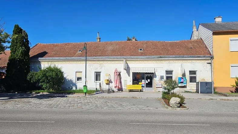 Langes, eingeschossiges Gebäude mit Ziegeldach und Ladenfront an einer Straße.