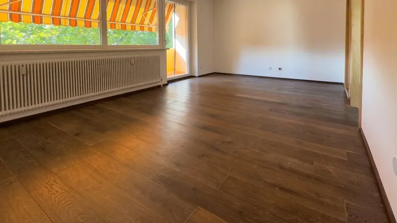 Helles Wohnzimmer mit dunklem Holzboden und Zugang zu einem Balkon mit Markise.