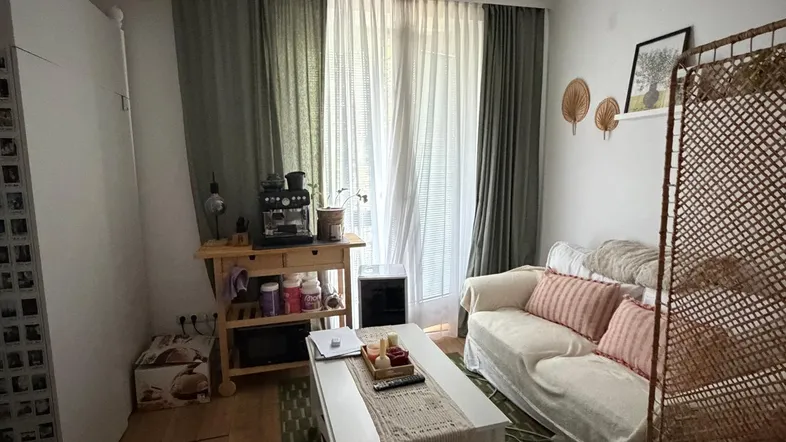 Helles Wohnzimmer mit Sofa, Couchtisch und Zugang zu einem Fenster mit Vorhängen.