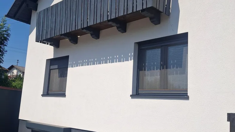 Fassade eines Hauses mit Balkon und dunklen Fensterrahmen.