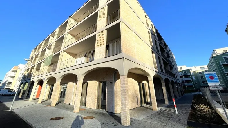Modernes Mehrfamilienhaus mit markanter Bogenarchitektur im Erdgeschoss und zahlreichen Balkonen.