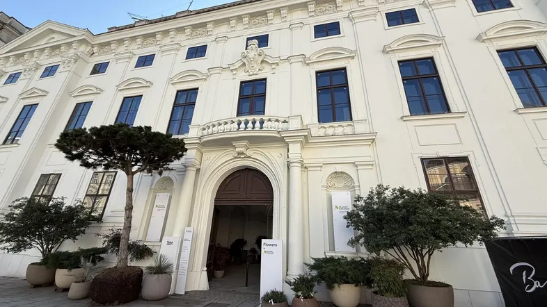 Klassisches weißes Gebäude mit eleganten Fenstern, einem Balkon über dem Eingang und dekorativen Pflanzen in Töpfen.