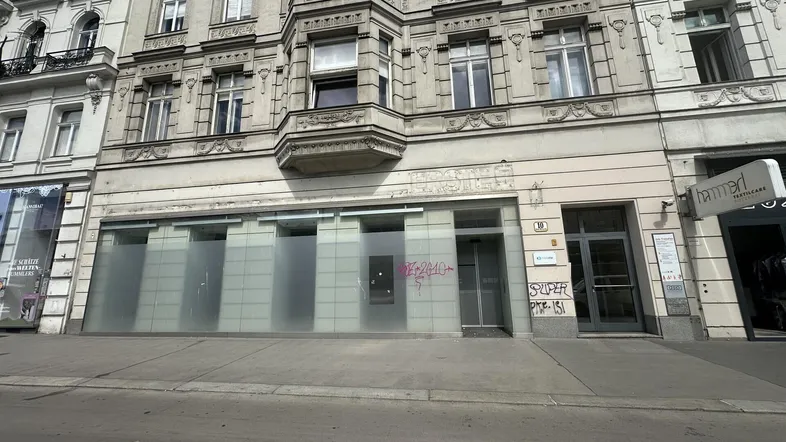 Vorderansicht eines historischen Gebäudes mit Ladengeschäft im Erdgeschoss und Graffiti an den Fenstern.