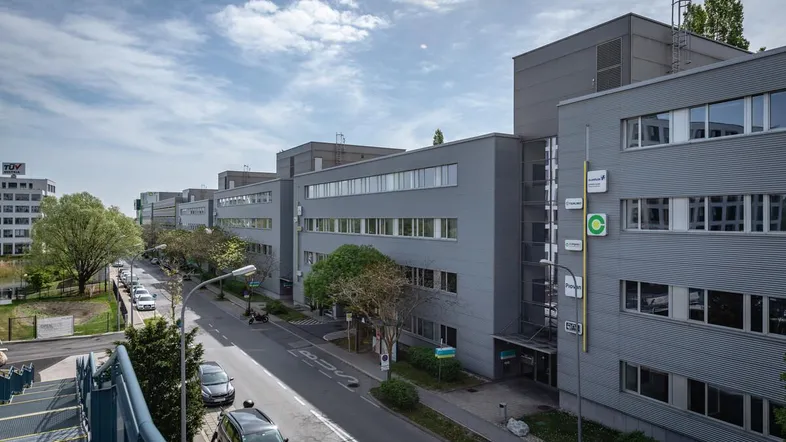 Mehrere moderne Bürogebäude entlang einer Straße unter bewölktem Himmel mit viel Grün.