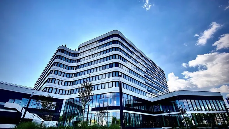 Modernes Bürogebäude mit geschwungenen Linien und vielen Glasflächen unter blauem Himmel.