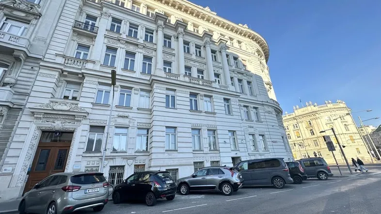 Historisches Gebäude mit klassischer Architektur und geparkten Autos an einer Stadtstraße.