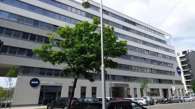 Modernes Bürogebäude mit vielen Fenstern und einem "aws start-up center" im Erdgeschoss, umgeben von Parkplätzen.