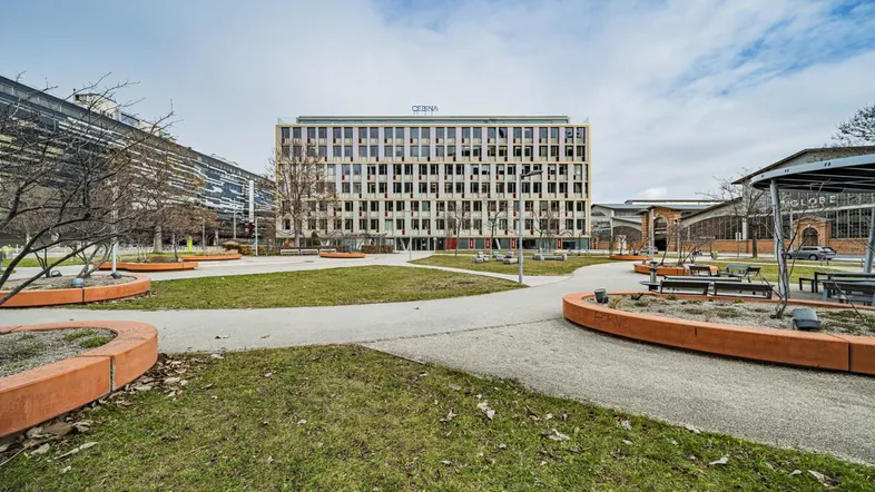 Modernes Bürogebäude mit vielen Fenstern, umgeben von einer gepflegten Grünfläche und Spazierwegen.
