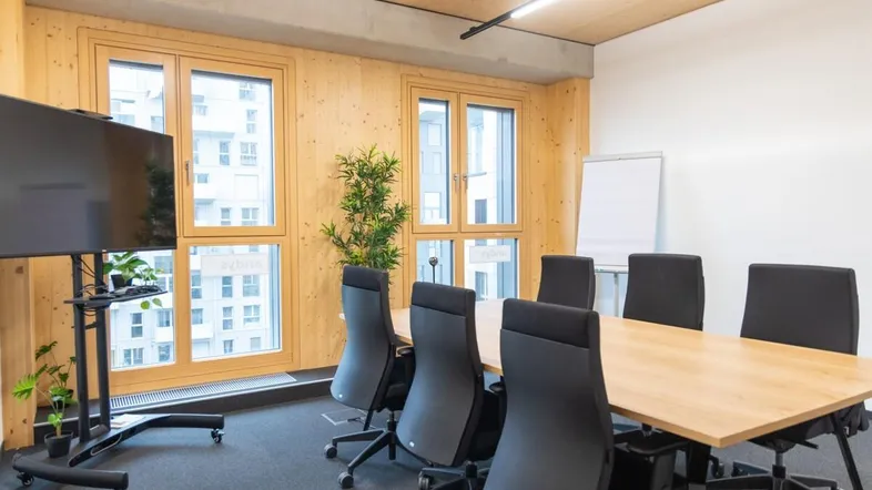 Moderner Konferenzraum mit Holzwänden, großem Bildschirm und Blick auf die umliegenden Gebäude.