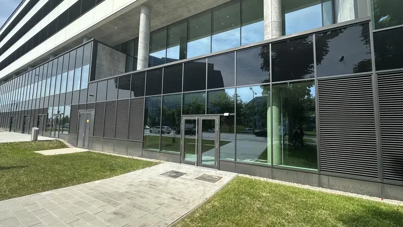 Moderne Bürogebäude-Fassade mit großen Glasflächen und Eingangsbereich, umgeben von Grünflächen und Gehwegen.