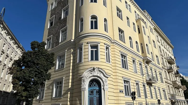 Historisches Eckgebäude mit gelber Fassade, blauer Eingangstür und dekorativen Elementen unter blauem Himmel.