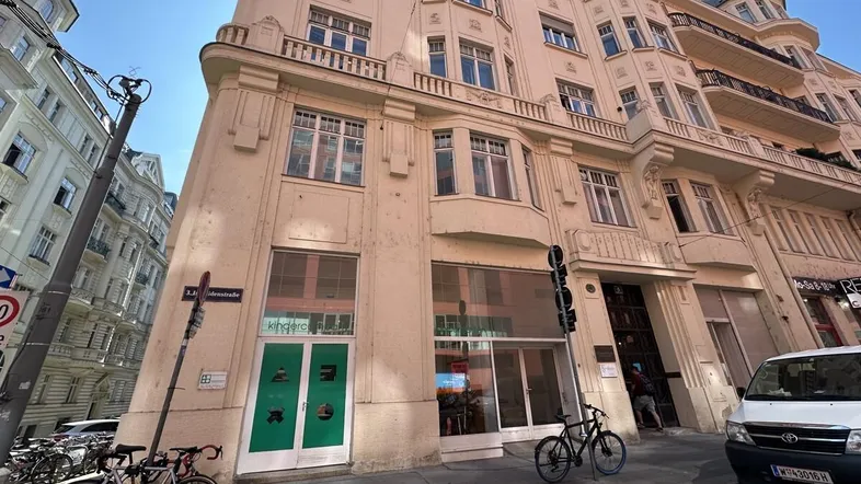 Historisches Gebäude mit eleganter Fassade an einer belebten Straße in der Stadt, unter strahlend blauem Himmel.