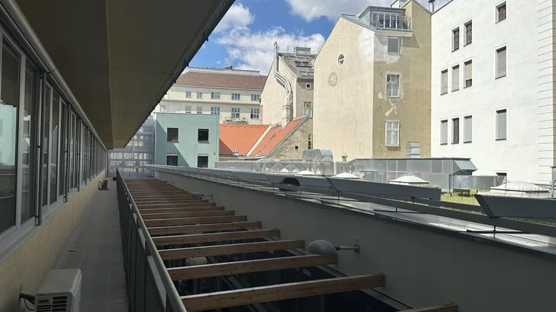 Blick über eine Dachterrasse im Bau mit Holzbalken und umliegenden Gebäuden unter blauem Himmel.