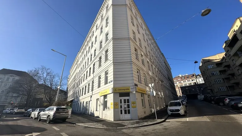 Eckgebäude mit mehreren Stockwerken und vielen Fenstern unter strahlend blauem Himmel an einer städtischen Straße.