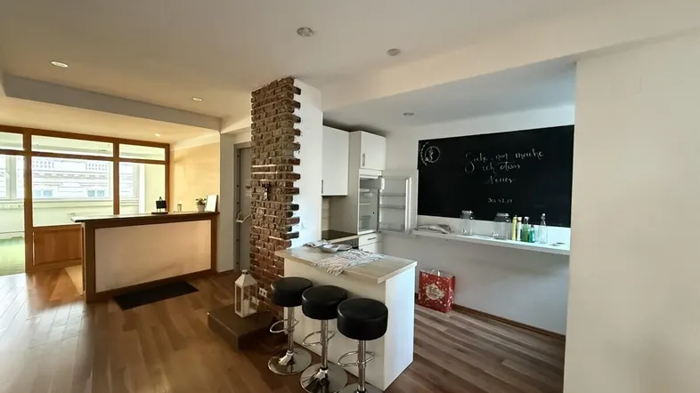 Offener Bereich mit Holzboden, einer Theke und einer kleinen Küchenzeile mit Kreidetafel, ideal für Empfänge.
