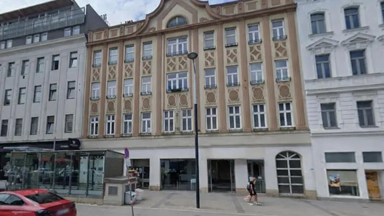 Historisches Gebäude mit reich verzierter Fassade und Geschäften im Erdgeschoss an einer belebten Straße.