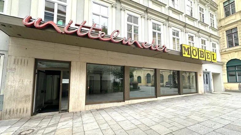 Gebäudefassade mit großen Schaufenstern und einem ehemaligen Ladenschild, das auf ein Möbelgeschäft hinweist.