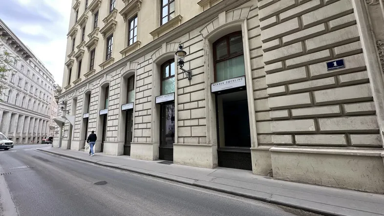 Historische Fassade eines Gebäudes an einer belebten Straße mit Geschäften im Erdgeschoss.