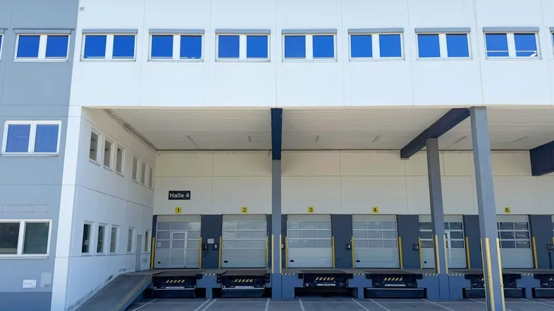 Moderne Lagerhalle mit mehreren Laderampen und Büroräumen im Obergeschoss unter blauem Himmel.