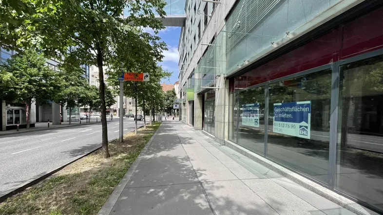 Moderne Geschäftsfassade mit großen Schaufenstern und "zu vermieten"-Schildern entlang einer belebten Straße.