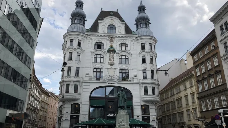 Historisches Gebäude mit markanter Architektur, Türmen und einer Statue auf einem belebten Stadtplatz.