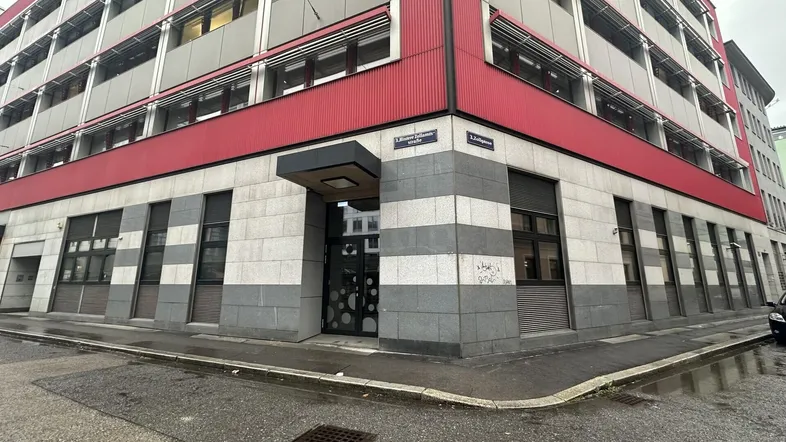 Modernes Bürogebäude mit roter und grauer Fassade an einer Straßenecke, gut gepflegt.