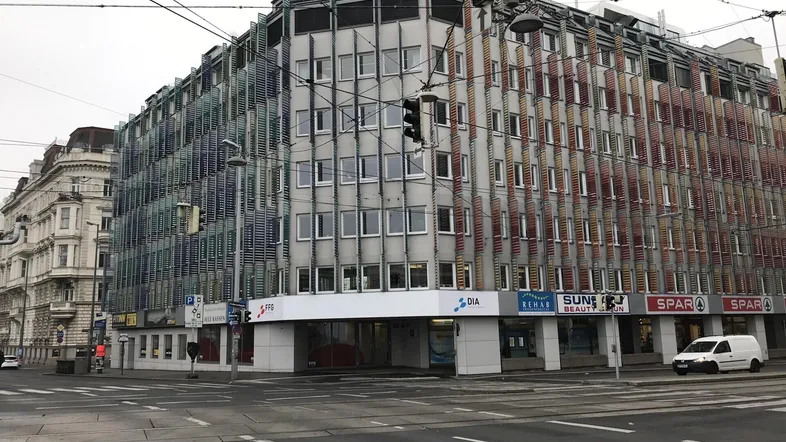 Großes Eckgebäude mit moderner Fassade und Geschäften im Erdgeschoss an einer belebten Kreuzung.
