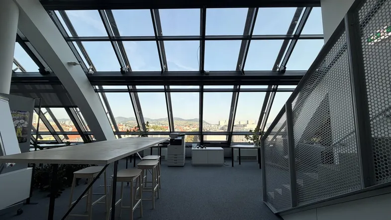 Großzügiger Bürobereich mit schrägen Glasfenstern und weitem Blick über die Stadtlandschaft.