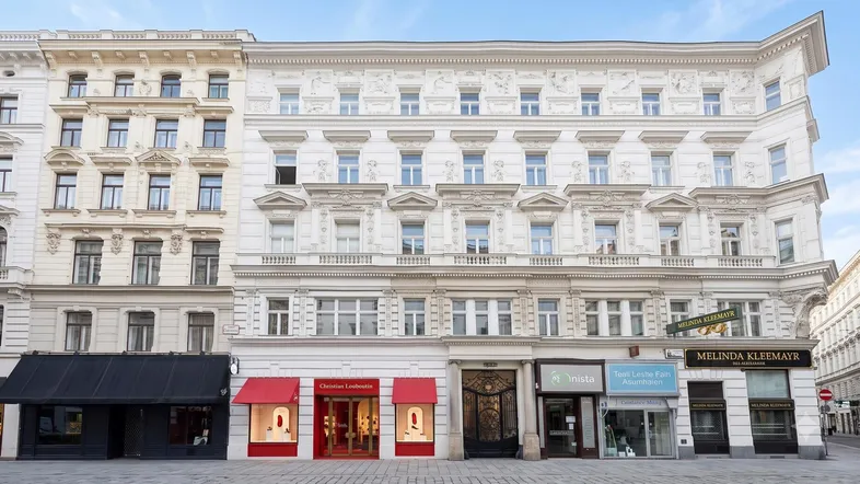Historische Fassade eines eleganten Gebäudes mit Geschäften im Erdgeschoss und vielen Fenstern.
