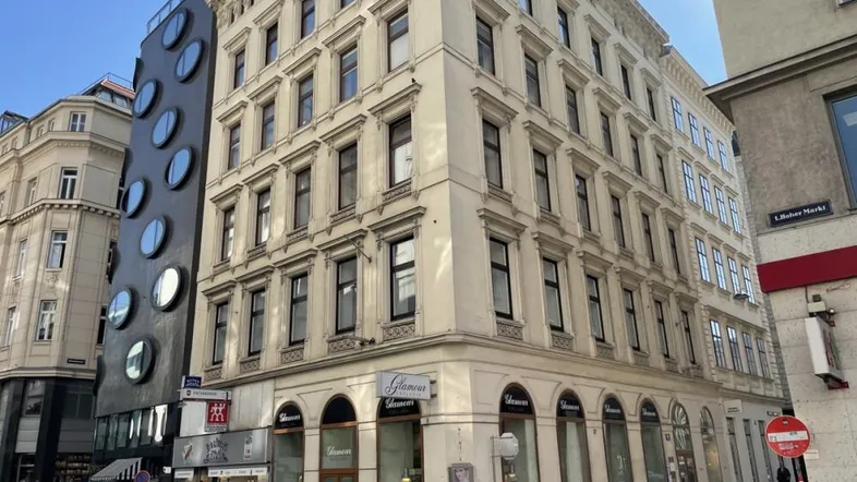 Historisches Gebäude an einer Straßenecke mit klassischer Fassade und einem modernen Anbau daneben.