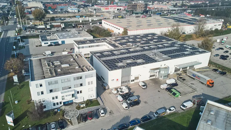 Luftaufnahme eines Gewerbegebiets mit mehreren Gebäuden, Parkplätzen und Solaranlagen auf den Dächern.